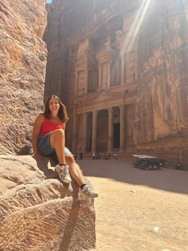 Abigail sits on a rock in the foreground with the entrance to Petra in the background